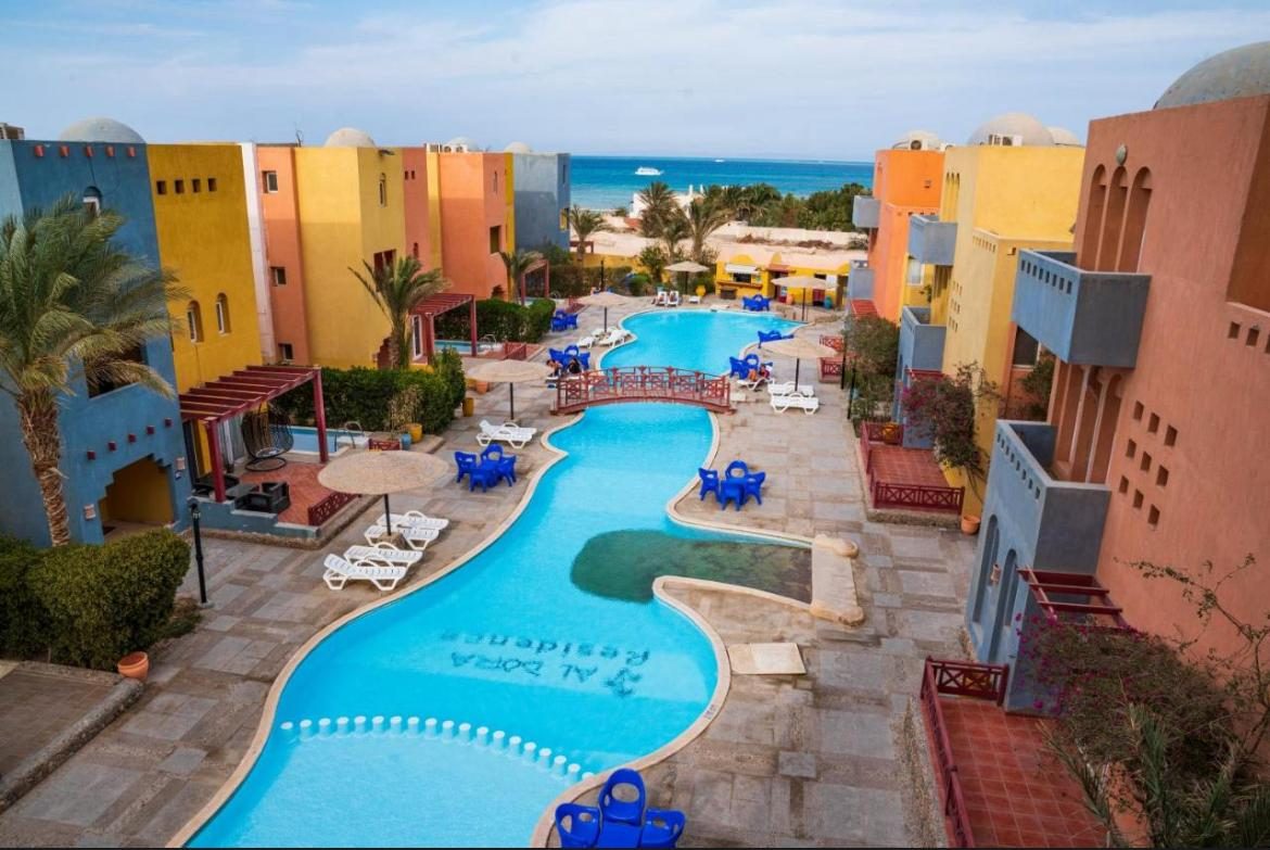 Al Dora Residence from above: colourful Nubian-style buildings around the long pool, Red Sea behind